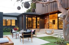 an outdoor living area with hanging chairs, tables and plants in front of the house