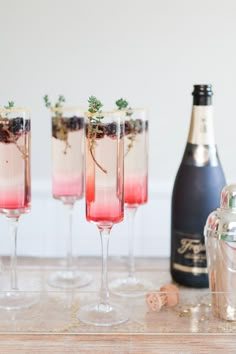 three champagne glasses filled with pink liquid and topped with greenery, next to a bottle of wine