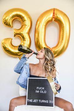 a woman drinking from a bottle while sitting in front of a sign that says 30th