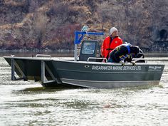 two men on a boat in the water with one man wearing a life jacket and another holding a dog