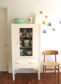 a white cabinet sitting next to a wooden chair in a room with wood flooring