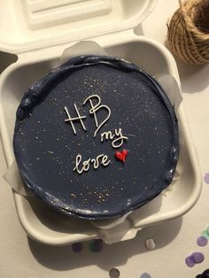 a blue cake with writing on it sitting in a white container next to some twine sprinkles