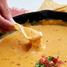 a person dipping tortilla chips into a bowl of soup with cheese and salsa