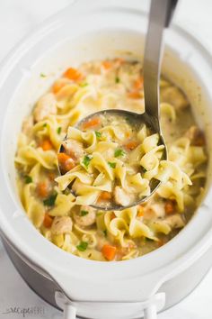 a ladle full of chicken noodle soup in a white crock pot with a spoon