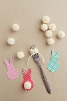 a fork and some paper bunny decorations on a table with white pom poms