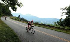 two bicyclists are riding down the road with mountains in the background