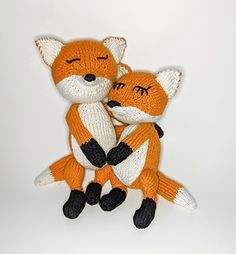 two knitted stuffed animals sitting next to each other on a white surface with eyes closed