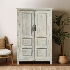 an old white cabinet next to a chair and potted plant