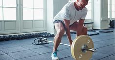 a man squatting down with a barbell in front of him on a gym floor