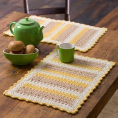 a wooden table topped with two green teapots next to a yellow and white crocheted placemat