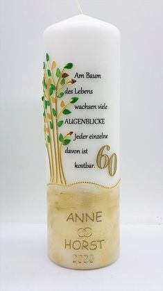 a white candle with green leaves on it and the words anne of horst written in gold