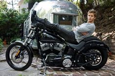 a man sitting on top of a motorcycle next to a airstream in the background