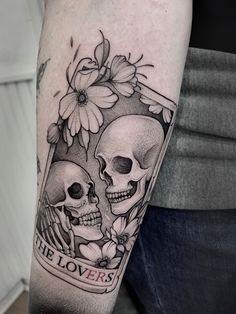 a couple of skulls sitting next to each other on a person's arm with flowers in the background