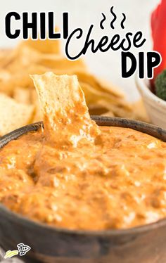 a bowl of chili cheese dip with tortilla chips on the side and a plate of vegetables in the background