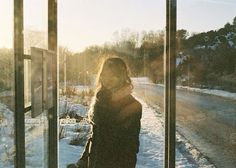 a woman standing in front of a window with snow on the ground and trees behind her