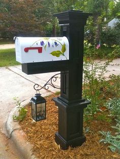 a mailbox with flowers painted on it is next to a lamp post in the grass