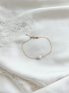 the bracelet has two pearls on it and is laying on top of a white sheet