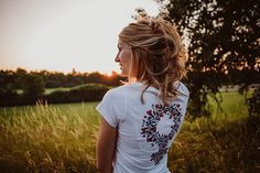 a woman standing in tall grass with the sun setting behind her and looking off into the distance