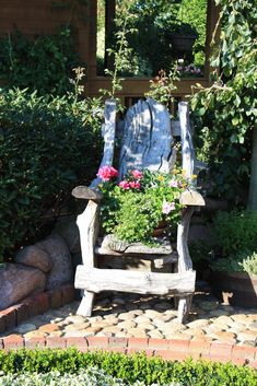 a wooden chair with flowers in it sitting next to a rock garden bed and shrubbery