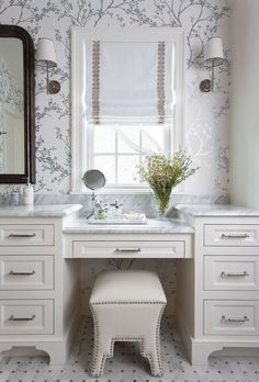 a white bathroom with floral wallpaper, vanity and stool in front of the mirror