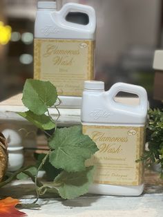 two gallon jugs of champagne wash sitting on a table next to leaves and flowers