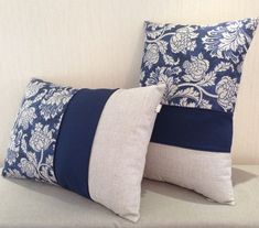 two blue and white pillows sitting on top of a couch next to each other in front of a wall