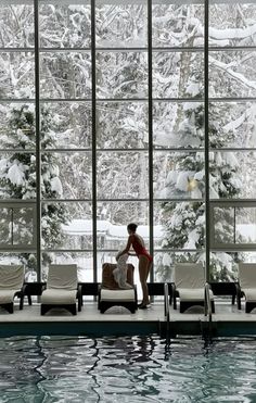 a woman sitting on the edge of a swimming pool next to a large glass window