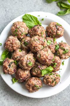 a white plate filled with meatballs and garnished with green leaves on top