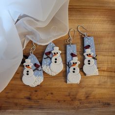 three snowmen are hanging from earrings on a table