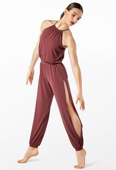 a woman in a maroon jumpsuit is standing with her legs crossed and one leg bent