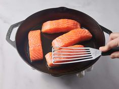 salmon being cooked in a skillet with tongs