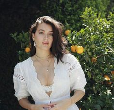 a woman standing in front of an orange tree with her hands on her hips and looking at the camera