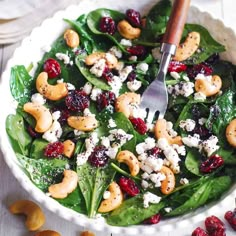 a white bowl filled with spinach salad and nuts