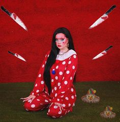 a woman sitting on the ground in front of a red wall with white polka dots