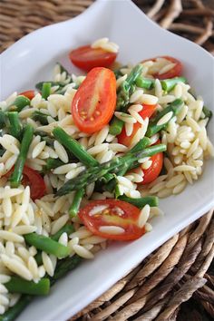 a white plate topped with pasta and veggies on top of a woven place mat