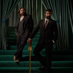 two men in suits are standing on the stairs with their canes and looking at the camera