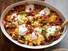 a white bowl filled with potatoes covered in cheese and bacon next to a wooden table