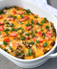 a casserole dish with cheese, tomatoes and green onions