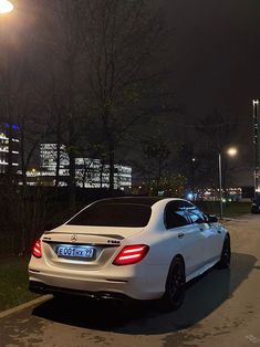 a white car is parked on the side of the road at night with street lights in the background