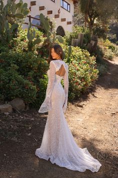 a woman in a white wedding dress standing on a dirt road near bushes and flowers