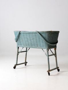 a blue basket sitting on top of a metal stand with wheels and no handle, in front of a white wall