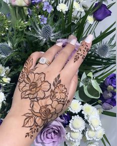 a woman's hand with henna on it next to flowers