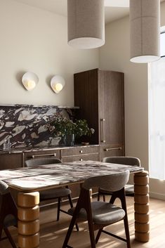 a dining room table surrounded by chairs in front of a wall with art work on it