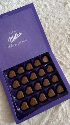 a purple box filled with chocolates sitting on top of a white carpeted floor