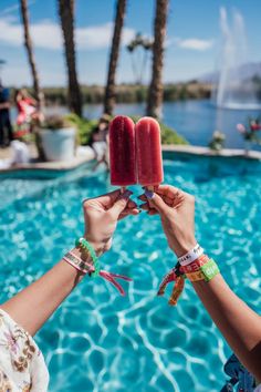 two people are holding up popsicles in front of a swimming pool with palm trees