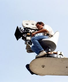 a man sitting on top of a camera attached to a crane with a bird flying in the background