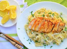 a white plate topped with chicken and pasta next to lemon wedges on a table