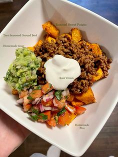 a hand holding a square white plate filled with taco salad and sweet potato wedges