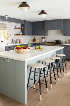 a kitchen with gray cabinets and white counter tops, an island in the middle has four stools