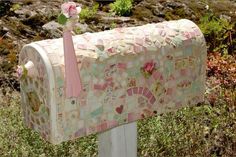 a mailbox decorated with mosaic tiles and pink ribbon tied to the front, sitting in some grass